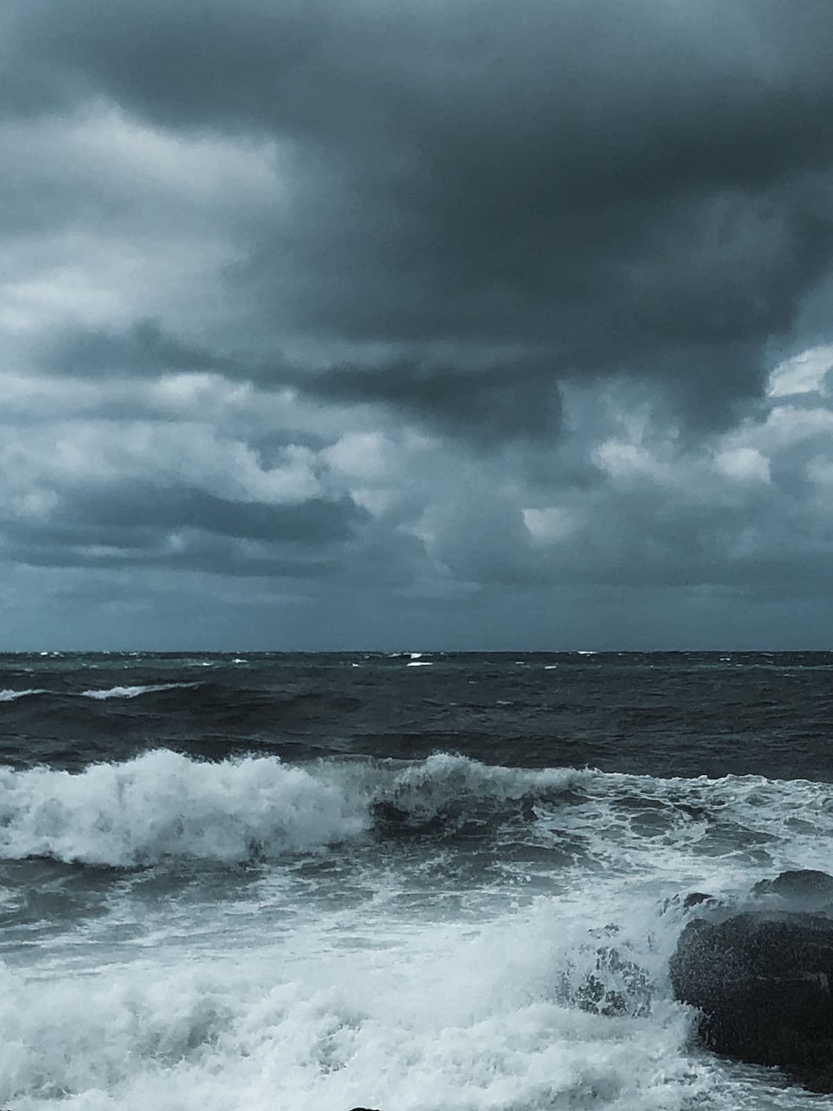 Dark storm clouds over open ocean with breaking waves on rocks, no structures or people in frame